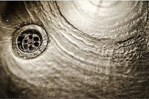 Circular metal drain with water ripples surrounding it.