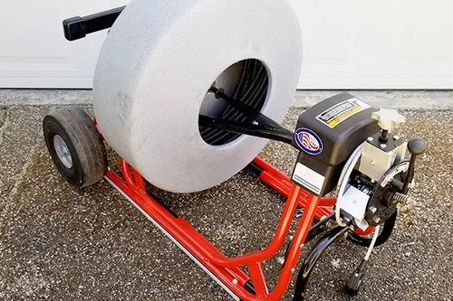 Sewer cleaning machine with a large gray drum and red frame.