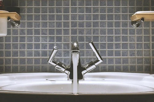 Chrome faucet with dual handles above a white sink, set against a blue tiled wall.