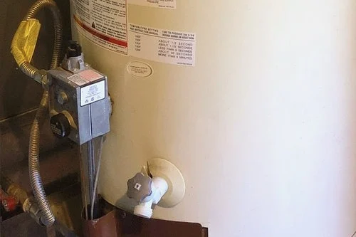 White cylindrical water heater with attached valves and pipes.