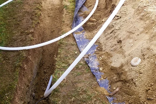 White pipes laid in a trench with dirt and grass.